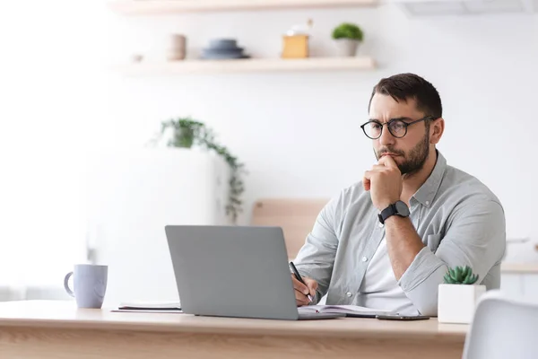 Concentrado maduro caucasiano homem de negócios com barba em óculos olhar para laptop no interior da cozinha — Fotografia de Stock