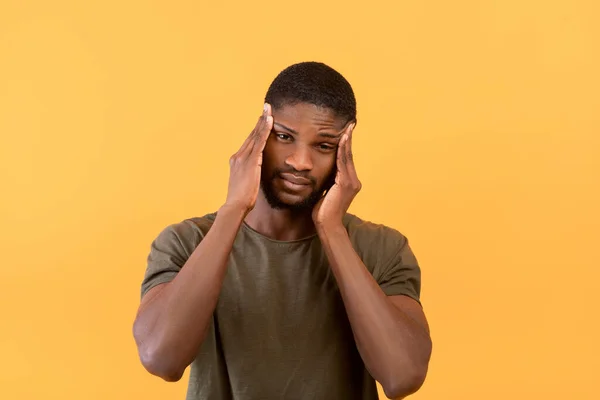 Ung afrikansk amerikansk kille som lider av huvudvärk, massera tempel för att bli av med smärta över gul bakgrund — Stockfoto