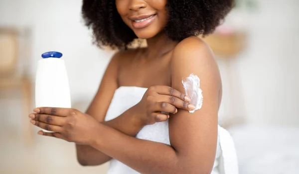 Mulher negra jovem irreconhecível aplicando loção em seu corpo, mimando a pele após o banho ou chuveiro em casa, close-up — Fotografia de Stock