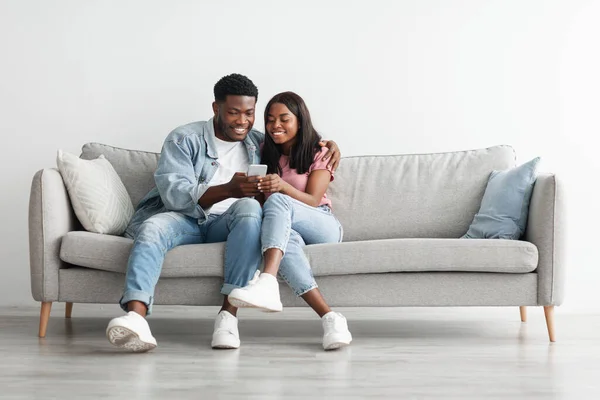 Africano casal americano sentado no sofá, usando celular — Fotografia de Stock