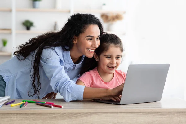 Любовь мать помогает своей милой дочери с домашней работой в Интернете во время дистанционного обучения — стоковое фото