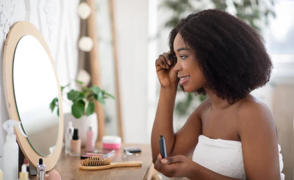 Ochtendschoonheidsroutine. Mooie zwarte dame aanbrengen mascara aan kaptafel, kijken in spiegel thuis, kopiëren ruimte — Stockfoto