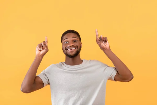 Emocionado hombre afroamericano apuntando con los dedos hacia arriba y sonriendo a la cámara mientras está de pie sobre el fondo amarillo — Foto de Stock