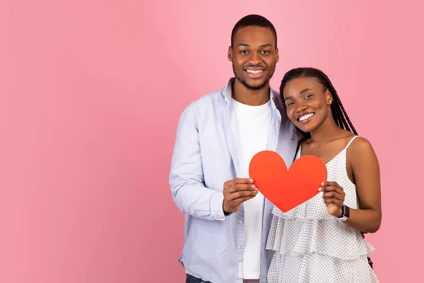 Joven pareja negra romántica abrazando y sosteniendo el corazón de papel rojo — Foto de Stock