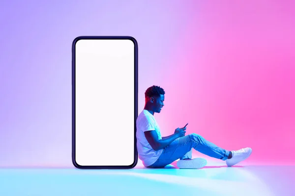 Genç siyahi adam boş ekranlı akıllı telefonun yanında oturuyor, yeni mobil uygulama ya da web sitesi reklamları yapıyor, — Stok fotoğraf