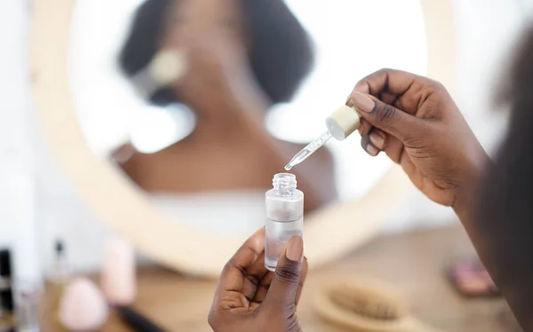 Närbild av ung svart kvinna som applicerar återfuktande serum inomhus — Stockfoto