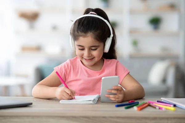 Lição Online. Menina em fones de ouvido usando Smartphone para estudo em casa — Fotografia de Stock