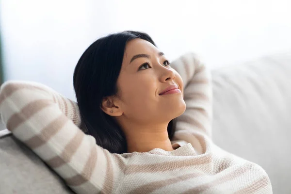 Portret van rustig mooi jong aziatisch vrouw leunend terug op comfortabele bank — Stockfoto