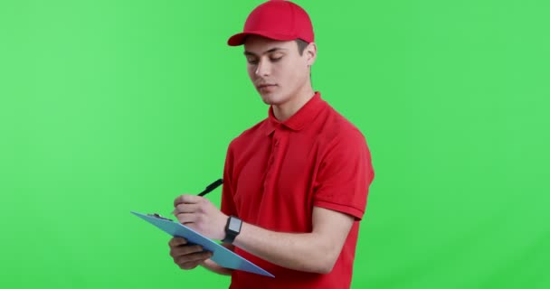 Young postman writing in check list, smiling at camera — Stock Video