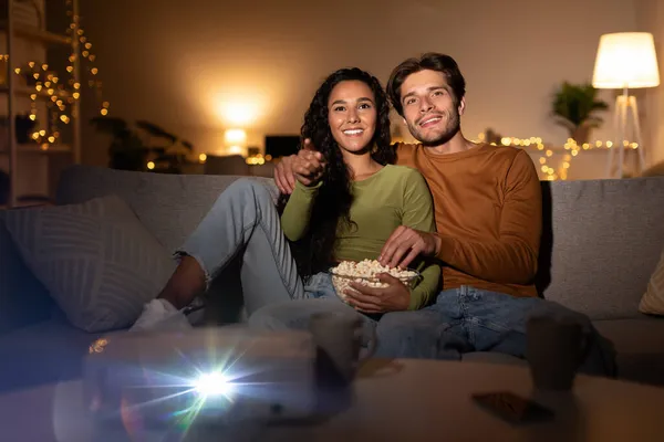 Glückliches Paar entspannt Film anschauen mit Projektor Popcorn essen drinnen — Stockfoto