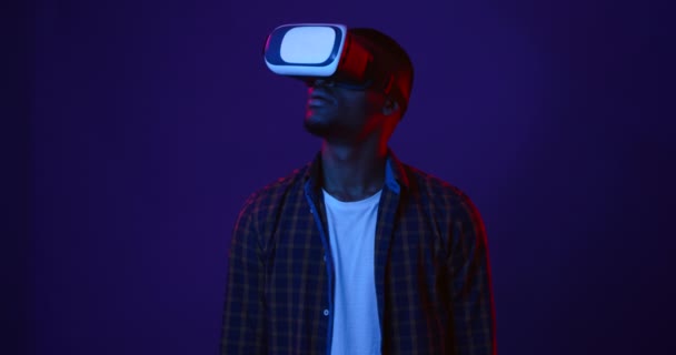 Futuristische technologieën. Afrikaans amerikaanse man het dragen van virtual reality bril kijken video, neon lichten achtergrond — Stockvideo