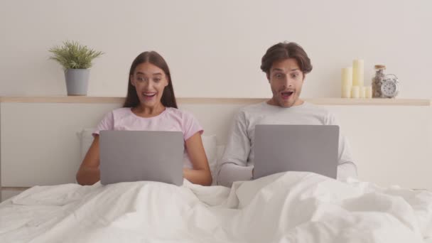Young surprised excited married man and woman web surfing on laptops, reading victory emails and looking at each other — Stock Video