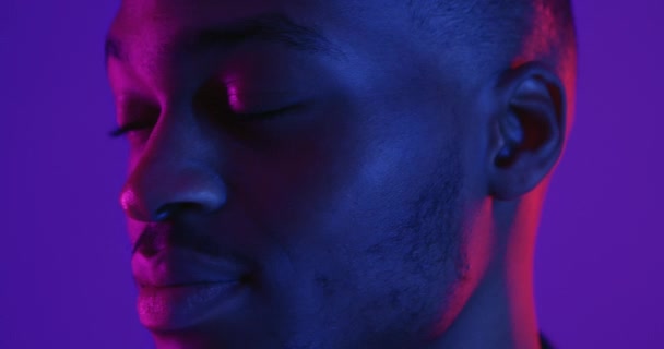 Jovem afro-americano positivo virando rosto para câmera e amplamente sorrindo, fundo luzes de néon — Vídeo de Stock