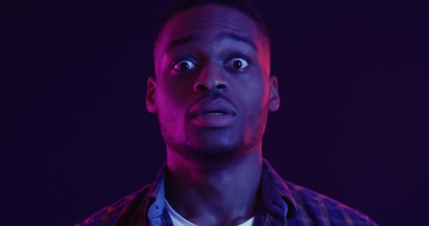 Shock expression. Close up of scared african american guy pulling back with big eyes, neon light background — Stock Video