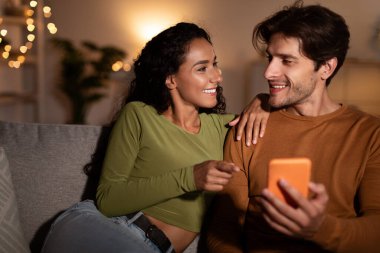 Cep telefonu kullanan bir çift, ev telefonunda parmağını gösteren bir eş.