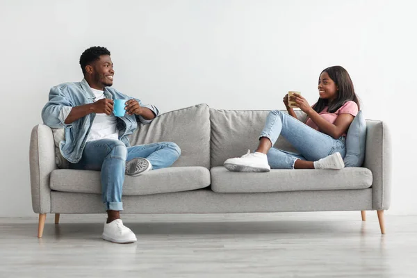 Afrikanskt amerikanskt par dricker kaffe sittandes på soffan — Stockfoto