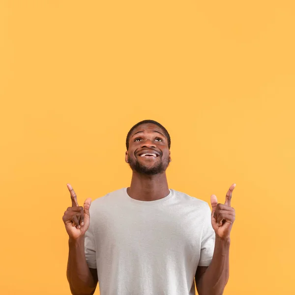 Kijk naar boven. Afro-Amerikaanse man wijzen en omhoog kijken naar kopieerruimte, demonstreren vrije plaats, gele achtergrond — Stockfoto