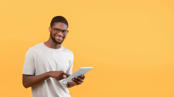 Portret szczęśliwego czarnego człowieka korzystającego z tabletu cyfrowego i uśmiechającego się do kamery, stojącego nad żółtym tłem, przestrzeń do kopiowania — Zdjęcie stockowe