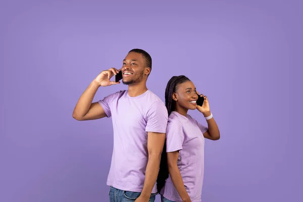 Pareja afroamericana hablando en smartphones, violeta studio wall — Foto de Stock