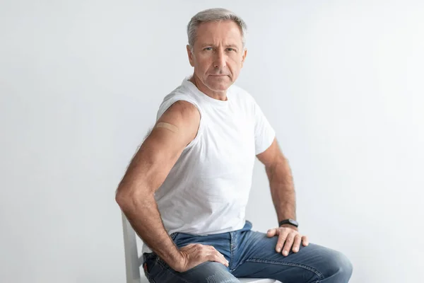 Homem sênior mostrando braço vacinado com gesso em fundo cinza — Fotografia de Stock