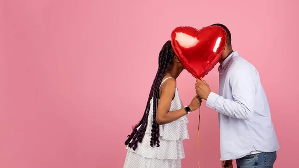 Romántica pareja negra besándose escondido detrás de rojo corazón globo — Foto de Stock