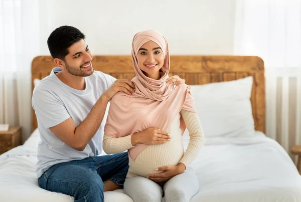 Junge liebende Muslima erwartet Paar beim Kuscheln, während sie Zeit miteinander verbringen, Mann massiert seine schwangere Frau auf den Schultern — Stockfoto