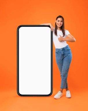 Beyaz, boş, akıllı telefon ekranına yaslanan kadın başparmağını kaldırıyor.