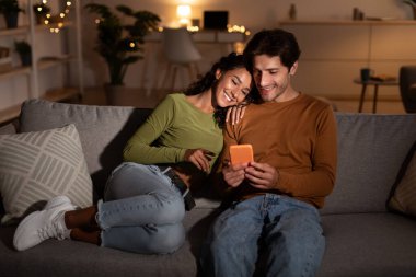 Evde koltukta oturan cep telefonu kullanan genç çift.