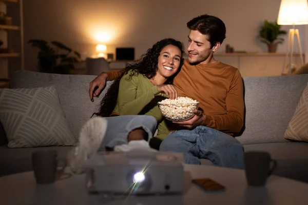 Ehemann und ehefrau beobachten film using projektor having spaß drinnen — Stockfoto