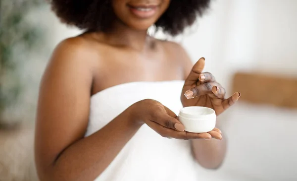 Vista cortada da jovem afro-americana usando creme hidratante, usando toalha de banho dentro de casa, close-up — Fotografia de Stock