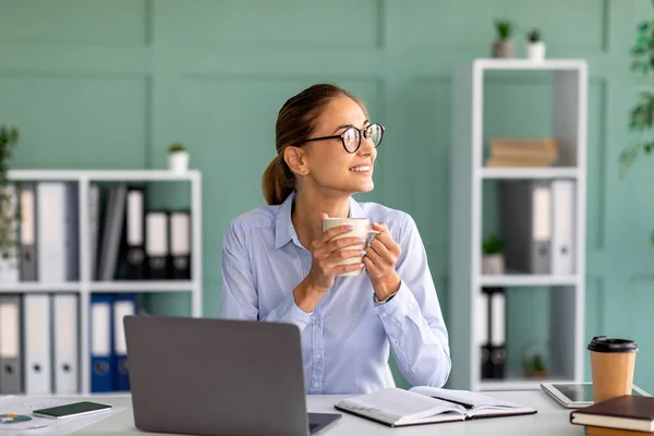 Kopje thee en chillen. Succesvolle jonge zakenvrouw die pauze heeft, warme drank drinkt en droomt op het werk — Stockfoto