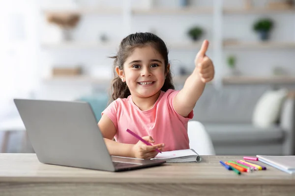 Menina árabe mostrando polegar para cima enquanto estuda com laptop em casa — Fotografia de Stock