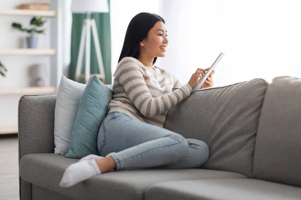 Retrato de bela mulher asiática sorridente descansando no sofá com tablet digital — Fotografia de Stock