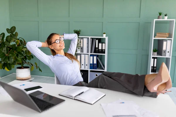 Empresária relaxada descuidada tendo tempo livre no local de trabalho, sentada em poltrona e colocando os pés na mesa — Fotografia de Stock