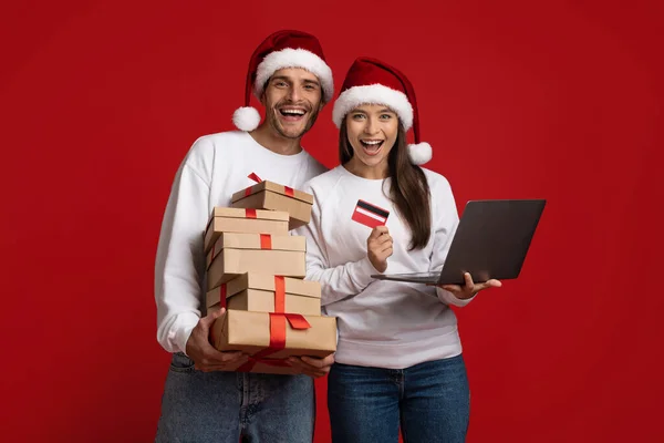 Christmas Shopping. Couple in santa hats with laptop, gifts and credit card — Stock Photo, Image