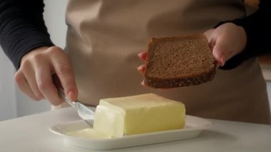 Mutfakta buğday ekmeğine tereyağı sürmüş bir kadın.
