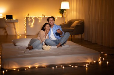 Neşeli Milenyum Çifti Televizyon seyrediyor ve evde patlamış mısır yiyor.