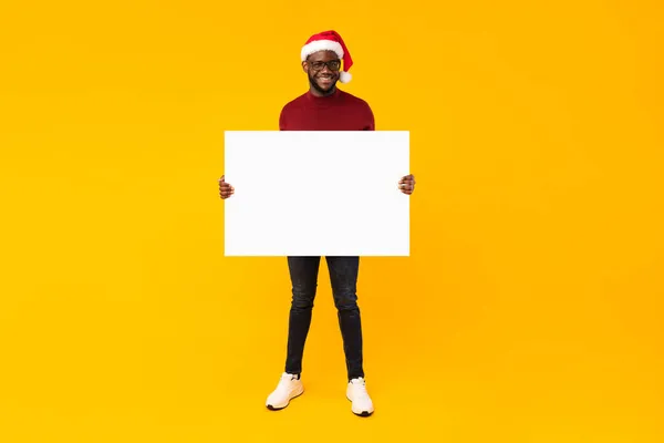 Chico negro mostrando cartel en blanco para la publicidad de Navidad, fondo amarillo — Foto de Stock