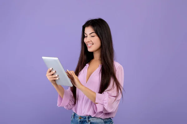 Dijital tablet kullanan mutlu Ermeni bayan, ekrana bakıyor ve gülümsüyor, mor arkaplan üzerinde duruyor, boşluğu kopyala — Stok fotoğraf