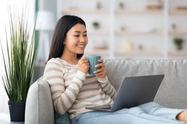 Weekend tijdverdrijf. Mooie Aziatische dame met behulp van laptop en het drinken van thee thuis — Stockfoto