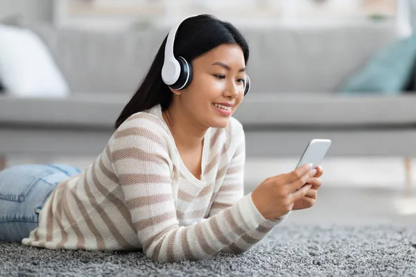 Retrato de joven dama coreana usando auriculares inalámbricos usando Smartphone en casa — Foto de Stock