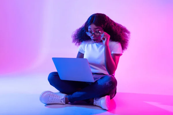 Deadline concept. Full length of surprised black woman using laptop computer, opening mouth in shock in neon light — Stock Photo, Image
