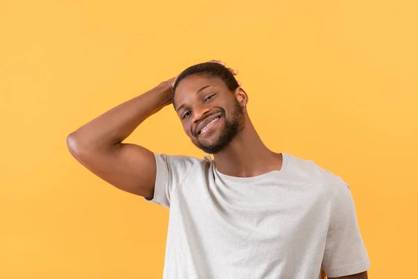 Porträt eines Afroamerikaners, der in die Kamera lächelt und die Haare mit der Hand berührt, posiert auf gelbem Hintergrund — Stockfoto