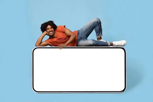Allegro ragazzo afroamericano rilassante su smartphone enorme, mockup — Foto Stock
