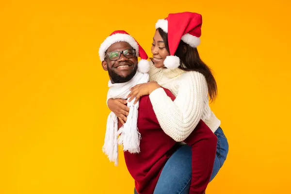 Marido afroamericano llevando esposa piggyback en Navidad, fondo amarillo — Foto de Stock