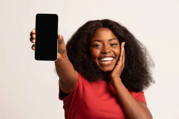 Gran aplicación. Sorprendida hembra negra demostrando Smartphone con pantalla grande en blanco — Foto de Stock