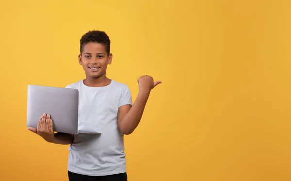 Wesoły czarny chłopiec z laptopem wskazującym na przestrzeń kopiowania — Zdjęcie stockowe