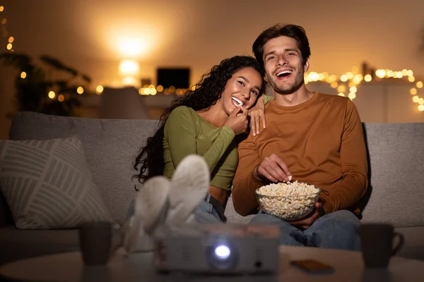 Cônjuges rindo assistindo filme de comédia comendo pipoca sentado dentro de casa — Fotografia de Stock