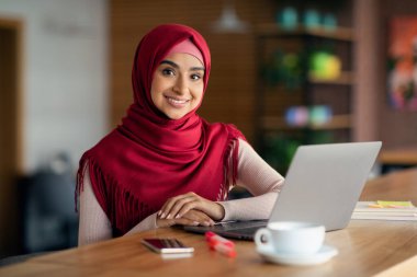 Neşeli Müslüman kadın modern laptop kullanıyor, kafenin içini.