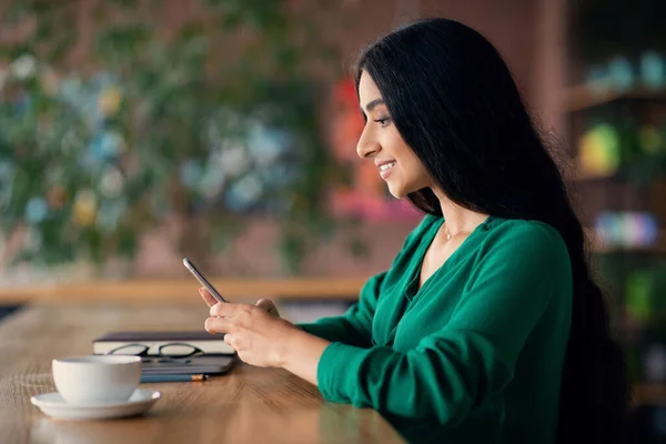 Zijaanzicht van aantrekkelijke Indiase langharige vrouw met behulp van smartphone — Stockfoto